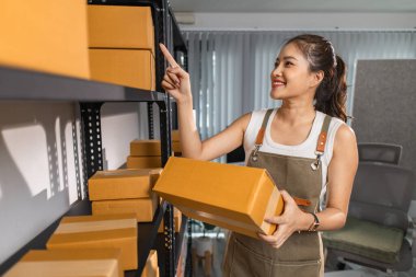 Bir bayan çalışan depodaki paket kutularını kontrol ediyor, bir depo müdürü raflardaki paket kutularını sayıyor, küçük bir online işletme sahibi bir depo odasında.