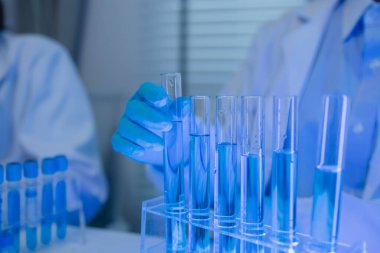 Laboratuvarda bilim adamları laboratuvar önlükleri, lastik eldivenler ve güvenlik gözlükleri takarken, iki kimyager sıvı haldeki kimyasalları test ediyor, kimyagerler laboratuarda çalışıyor.