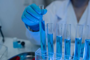 Laboratuvarda bilim adamları laboratuvar önlükleri, lastik eldivenler ve güvenlik gözlükleri takarken, iki kimyager sıvı haldeki kimyasalları test ediyor, kimyagerler laboratuarda çalışıyor.