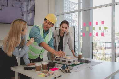 Mimar ve ekibi, bina modeli, mühendis ve takım çalışması ile planlardaki yapısal planların nasıl kontrol edileceği konusunda beyin fırtınası yapmak için inşaat yöneticisiyle görüşüyor.