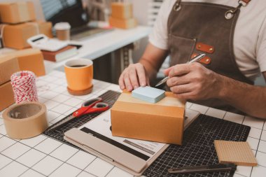 Küçük bir çevrimiçi işletme sahibi müşterilere göndermeden önce doğruluk için kutucukları işaretliyor, paket, bir çalışan müşterilere gönderilmek üzere ürünleri kutulara koyuyor