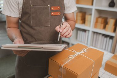 Çalışan, müşterilere nakliyeye hazırlanmak için ürünleri kutulara koyuyor, küçük bir online işletme sahibi müşterilere göndermeden önce doğruluk için kutucukları işaretliyor, paket,