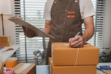 Çalışan, müşterilere nakliyeye hazırlanmak için ürünleri kutulara koyuyor, küçük bir online işletme sahibi müşterilere göndermeden önce doğruluk için kutucukları işaretliyor, paket,