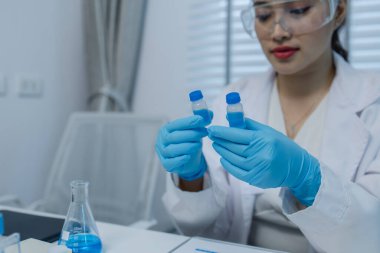 Bir kadın bilim adamı laboratuvarda çalışıyor, bir kimyager laboratuarda sıvı örneği test ediyor, laboratuarda çalışırken önlük giyiyor, test tüpü, bilimsel ekipman.