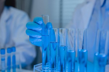 Laboratuvarda bilim adamları laboratuvar önlükleri, lastik eldivenler ve güvenlik gözlükleri takarken, iki kimyager sıvı haldeki kimyasalları test ediyor, kimyagerler laboratuarda çalışıyor.