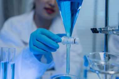 Bir kadın kimyager laboratuvarda çeşitli sıvı bileşiklerini test ediyor, bir bilim adamı bu gelişim üzerine araştırma yapıyor, laboratuvar, test tüpü ve bilimsel ekipmanlarda çalışırken önlük giyiyor.