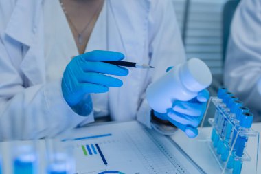 Bir kadın kimyager laboratuvarda çeşitli sıvı bileşiklerini test ediyor, bir bilim adamı bu gelişim üzerine araştırma yapıyor, laboratuvar, test tüpü ve bilimsel ekipmanlarda çalışırken önlük giyiyor.