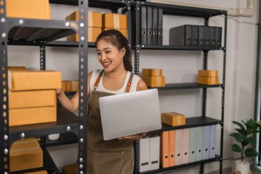 Paketleyici, bir müşteriye teslim edilmeden önce paketin durumunu kontrol eder, küçük bir işletme sahibi bir depodaki kutuları inceler, raflarla dolu bir depo ve paket