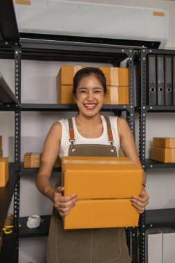 Paketleyici, bir müşteriye teslim edilmeden önce paketin durumunu kontrol eder, küçük bir işletme sahibi bir depodaki kutuları inceler, raflarla dolu bir depo ve paket