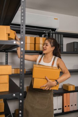 Paketleyici, bir müşteriye teslim edilmeden önce paketin durumunu kontrol eder, küçük bir işletme sahibi bir depodaki kutuları inceler, raflarla dolu bir depo ve paket