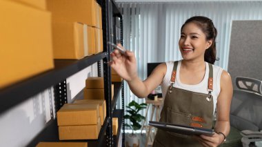 Paketleyici, bir müşteriye teslim edilmeden önce paketin durumunu kontrol eder, küçük bir işletme sahibi bir depodaki kutuları inceler, raflarla dolu bir depo ve paket