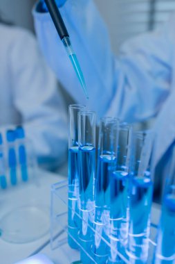 Laboratuvarda bilim adamları laboratuvar önlükleri, lastik eldivenler ve güvenlik gözlükleri takarken, iki kimyager sıvı haldeki kimyasalları test ediyor, kimyagerler laboratuarda çalışıyor.