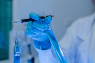 Bir kadın kimyager laboratuvarda çeşitli sıvı bileşiklerini test ediyor, bir bilim adamı bu gelişim üzerine araştırma yapıyor, laboratuvar, test tüpü ve bilimsel ekipmanlarda çalışırken önlük giyiyor.