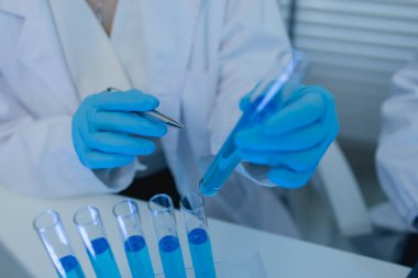 Bir kadın kimyager laboratuvarda çeşitli sıvı bileşiklerini test ediyor, bir bilim adamı bu gelişim üzerine araştırma yapıyor, laboratuvar, test tüpü ve bilimsel ekipmanlarda çalışırken önlük giyiyor.