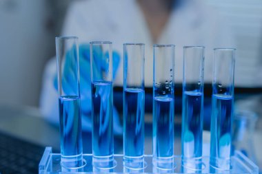 Bir kadın kimyager laboratuvarda çeşitli sıvı bileşiklerini test ediyor, bir bilim adamı bu gelişim üzerine araştırma yapıyor, laboratuvar, test tüpü ve bilimsel ekipmanlarda çalışırken önlük giyiyor.