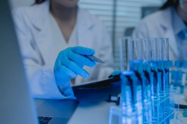 Bir kadın kimyager laboratuvarda çeşitli sıvı bileşiklerini test ediyor, bir bilim adamı bu gelişim üzerine araştırma yapıyor, laboratuvar, test tüpü ve bilimsel ekipmanlarda çalışırken önlük giyiyor.