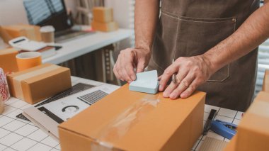 Çalışan, müşterilere nakliyeye hazırlanmak için ürünleri kutulara koyuyor, küçük bir online işletme sahibi müşterilere göndermeden önce doğruluk için kutucukları işaretliyor, paket,
