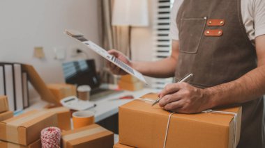 Çalışan, müşterilere nakliyeye hazırlanmak için ürünleri kutulara koyuyor, küçük bir online işletme sahibi müşterilere göndermeden önce doğruluk için kutucukları işaretliyor, paket,