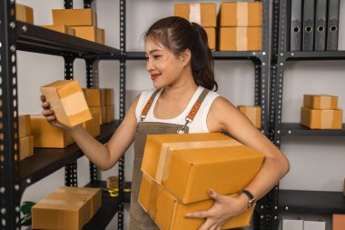 Paketleyici, bir müşteriye teslim edilmeden önce paketin durumunu kontrol eder, küçük bir işletme sahibi bir depodaki kutuları inceler, raflarla dolu bir depo ve paket