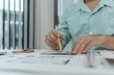 Bir mimar, mimari yapı planları üzerinde çalışırken hassasiyet ve detaylara odaklanarak beyaz bir masanın üzerine çizgiler çizmek için metal bir üçgen cetvel kullanır..