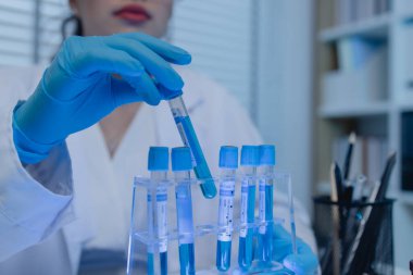 Bir kadın bilim adamı laboratuvarda çalışıyor, bir kimyager laboratuarda sıvı örneği test ediyor, laboratuarda çalışırken önlük giyiyor, test tüpü, bilimsel ekipman.