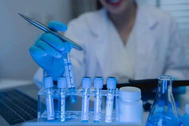 Bir kadın kimyager laboratuvarda çeşitli sıvı bileşiklerini test ediyor, bir bilim adamı bu gelişim üzerine araştırma yapıyor, laboratuvar, test tüpü ve bilimsel ekipmanlarda çalışırken önlük giyiyor.