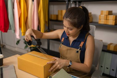 Genç bayan girişimci paketini bant ile dikkatlice mühürlüyor, mal siparişlerini hazırlıyor, başarılı online giyim işi için ev işindeki sevkiyat ve teslimatı yönetiyor..
