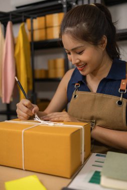 Genç bayan girişimci bir paket etiketinin üzerine bir nakliye adresi yazarak ev ofisine teslimat için bir paket hazırlıyor. Online bir iş yürütüyor ve müşterilere sevkiyat düzenliyor..