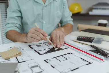 Bir mimar, mimari yapı planları üzerinde çalışırken hassasiyet ve detaylara odaklanarak beyaz bir masanın üzerine çizgiler çizmek için metal bir üçgen cetvel kullanır..