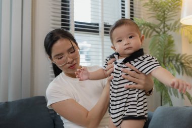 Genç bir anne, bebeğini sevgiyle kucaklar ve bir kanepede emzirir. Erken çocukluk ve aile hayatının anne bakımını, bağlarını ve besleyici anlarını sembolize eder..