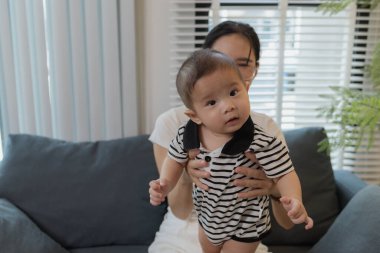 Genç bir anne, bebeğini sevgiyle kucaklar ve bir kanepede emzirir. Erken çocukluk ve aile hayatının anne bakımını, bağlarını ve besleyici anlarını sembolize eder..