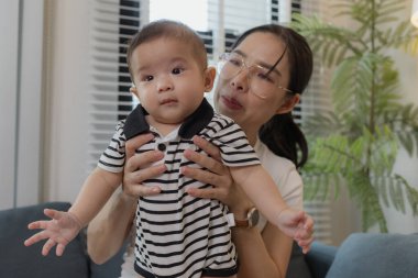 Genç bir anne, bebeğini sevgiyle kucaklar ve bir kanepede emzirir. Erken çocukluk ve aile hayatının anne bakımını, bağlarını ve besleyici anlarını sembolize eder..