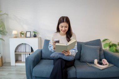 Genç bir kadın kanepede rahatça oturur, elinde kahve fincanı tutarken defter okur. Rahatlamış ve odaklanmış görünüyor. Evde sakin bir çalışma ya da planlama anının tadını çıkarıyor..
