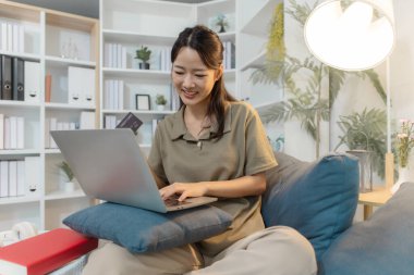 Genç bir kadın elinde bir kredi kartı tutarken bir dizüstü bilgisayar kullanarak kanepeye oturur ve çevrimiçi ödeme yaparken gülümser. Sahne dijital yaşam tarzı, modern finans ve güvenli alışveriş alışkanlıklarını yansıtıyor.