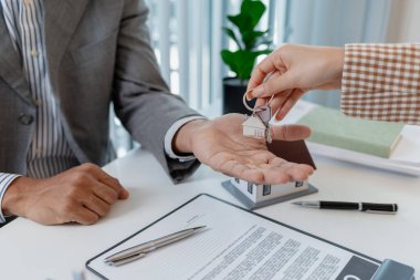 İki iş adamı emlak yatırımını tartışıyor, emlak sözleşmeleri imzalıyor ve ev modellerini gözden geçiriyor, konut satışlarını, finansmanı ve başarılı anlaşmaları sembolize ediyor.