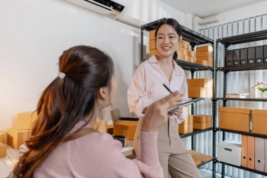 Küçük bir iş ofisinde birlikte çalışan iki genç kadın paketleri düzenliyor, belgeleri gözden geçiriyor ve gülümseyerek görevler planlıyorlar. Sahne takım çalışması, üretkenlik ve modern girişimciliği yansıtır