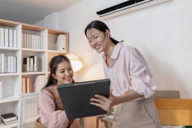 Küçük bir iş ofisinde birlikte çalışan iki genç kadın paketleri düzenliyor, belgeleri gözden geçiriyor ve gülümseyerek görevler planlıyorlar. Sahne takım çalışması, üretkenlik ve modern girişimciliği yansıtır