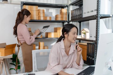 Küçük bir iş ofisinde birlikte çalışan iki genç kadın paketleri düzenliyor, belgeleri gözden geçiriyor ve gülümseyerek görevler planlıyorlar. Sahne takım çalışması, üretkenlik ve modern girişimciliği yansıtır