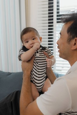 Bebeğini kucağında tutan bir babanın şefkatli anı. Bebek merakla ve güvenle yukarı bakıyor. Sıcak etkileşim aile sevgisini, yakınlaşmayı ve ebeveyn bakımını yansıtır..