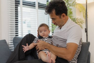 Bebeğini kucağında tutan bir babanın şefkatli anı. Bebek merakla ve güvenle yukarı bakıyor. Sıcak etkileşim aile sevgisini, yakınlaşmayı ve ebeveyn bakımını yansıtır..