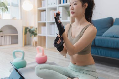 Genç bir kadın evde egzersiz yapıyor, yoga yapıyor ve halterleri ve dambılları ile egzersiz yapıyor. Egzersiz rutinini odaklanma ve kararlılıkla takip ediyor..