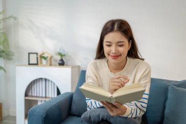 Evdeki kanepede oturan genç bir kadın elinde bir kitapla rahatlıyor. Okumaktan zevk alırken sakin ve mutlu görünüyor, boş zamanı ve huzurlu yaşam tarzını temsil ediyor..