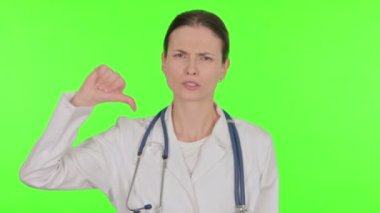 Thumbs Down by Young Female Doctor on Green Background 