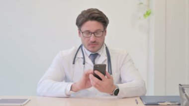 Klinikte akıllı telefon kullanan orta yaşlı bir doktor.