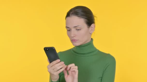 黄色の背景にスマートフォンで若い女性の損失 — ストック動画
