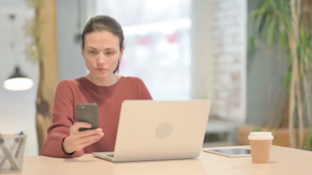Молода Жінка Користується Смартфоном Користуючись Ноутбуком — стокове відео