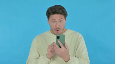 Handsome Young Man Loss on Smartphone on Blue Background