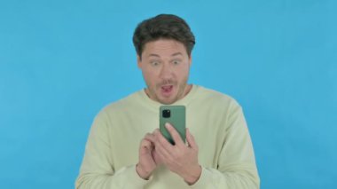 Handsome Young Man Celebrating on Smartphone on Blue Background
