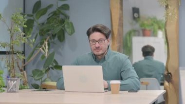 Middle Aged Businessman Smiling at Camera while using Laptop
