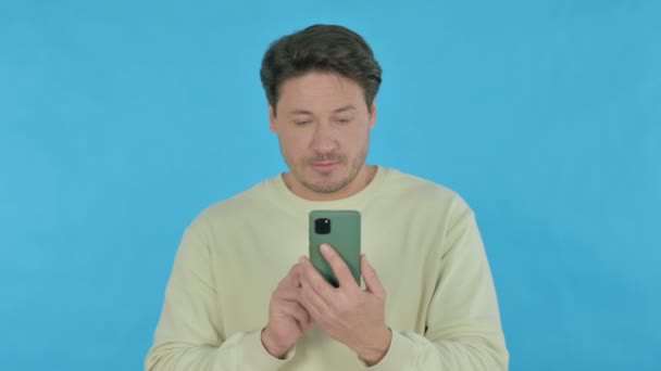Handsome Young Man Browsing Smartphone Blue Background — Vídeo de stock